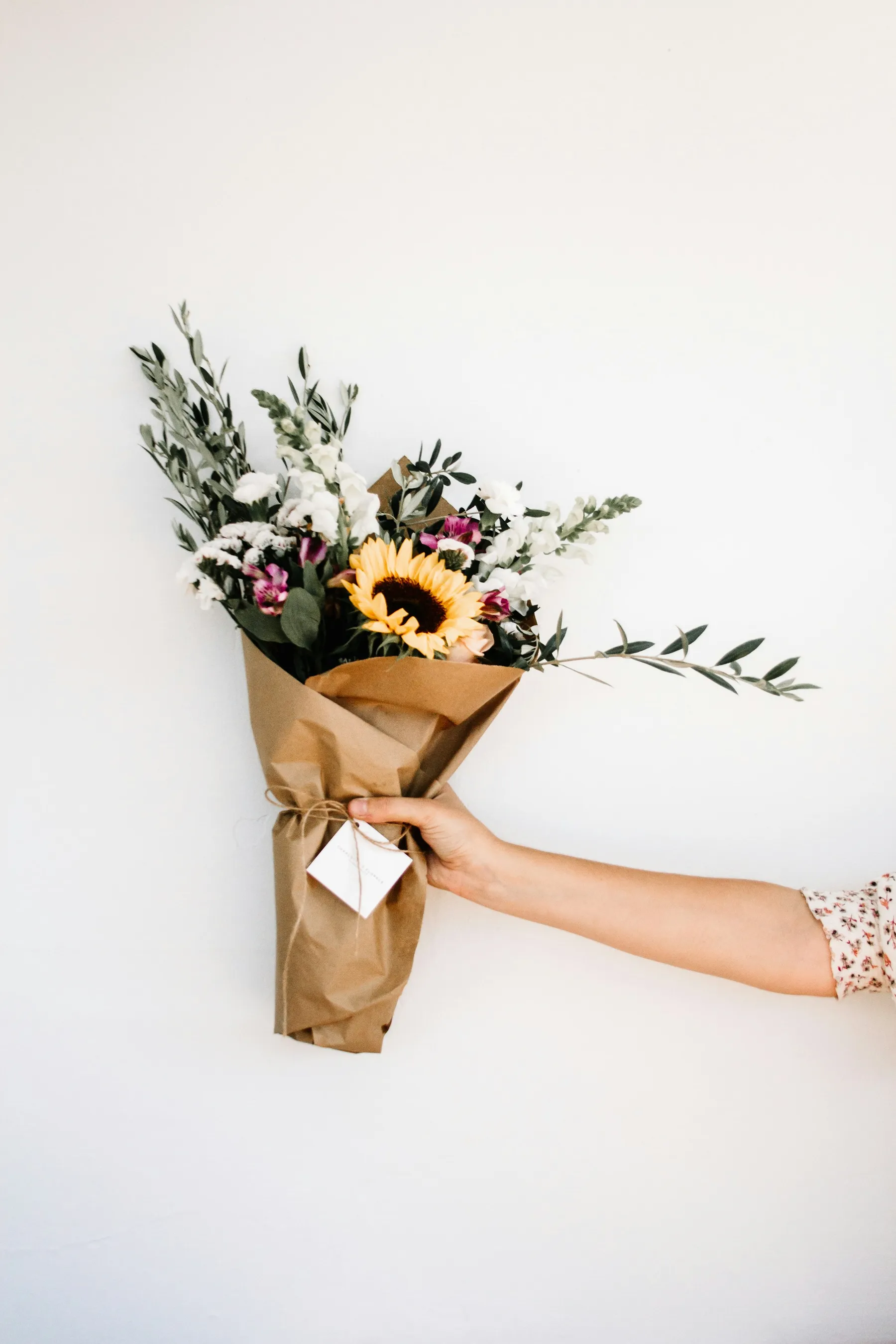Mano entregando un ramo de flores envuelto en papel kraft